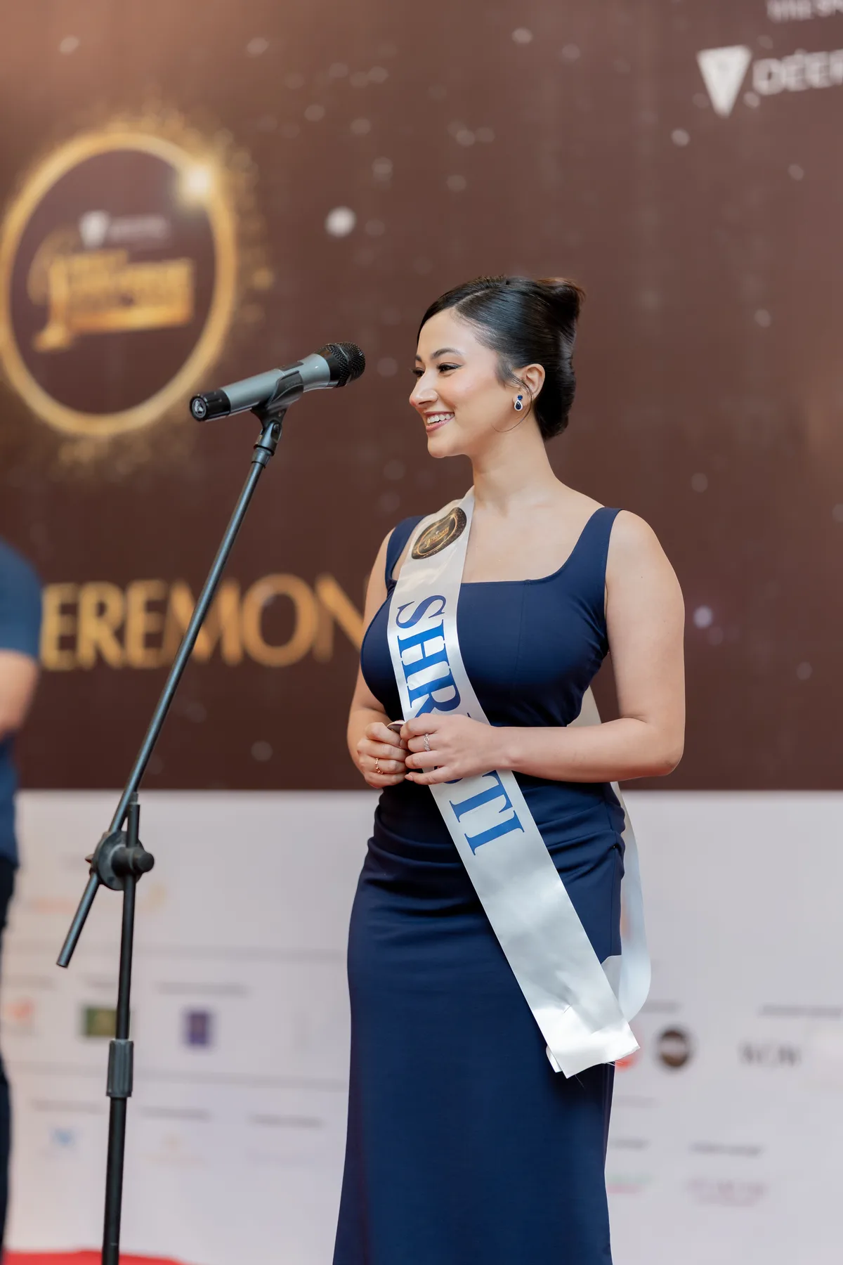 Shristi Bhusal speaking at the Miss Universe Nepal 2026 ceremony with contestant sash